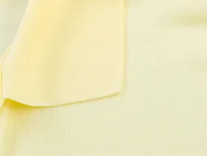 Macro dettaglio della trama del tessuto a maglia giallo chiaro di una polo a maniche lunghe