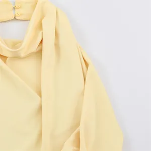 Detailed view of pale yellow top featuring elegant draped cowl neckline and button closure