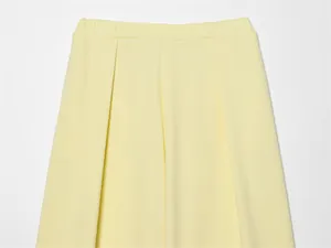 Dettaglio ravvicinato di pantaloni giallo chiaro con vita elastica ed eleganti pieghe frontali.