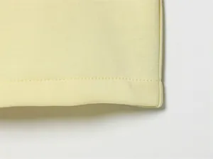 Primo piano dettagliato che mostra la doppia cucitura precisa su tessuto in maglia giallo