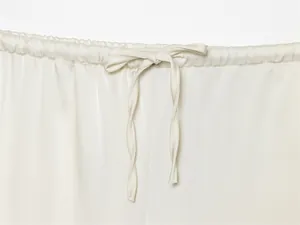 Detalle de la cintura elástica y el cordón de ajuste de estos pantalones de satén color crema.