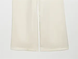 Primer plano de pantalones de satén crema con pernera ancha mostrando textura y dobladillo