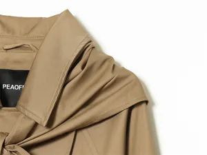 Detalle de gabardina corta color caqui con bufanda a juego y etiqueta de marca al cuello
