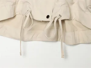 Vue détaillée de l'ourlet d'une veste d'été avec cordons réglables et bouton-pression en métal.