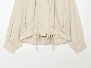 Détail d'une veste beige clair à manches lanterne avec cordon de serrage et bouton-pression
