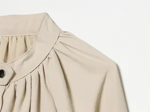 Détail de l'épaule plissée et du col montant sur la veste d'été beige à manches lanternes