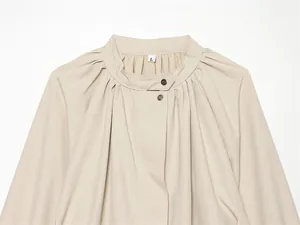 Détail d'une veste beige à manches lanternes avec col montant et boutons-pression
