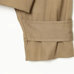 Primer plano de la manga de una gabardina corta caqui con correa ajustable y tejido sarga.