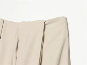 Détail d'un pantalon d'été beige montrant la taille plissée et la texture du tissu.