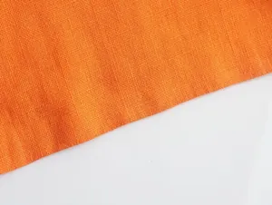 Close-up macro detail of breathable orange linen fabric showing fine natural weave texture
