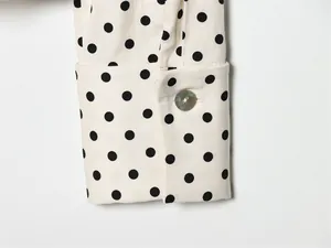 Detailopname van een hemdsmanchet met zwarte stippen en een parelmoeren knoop erbij.