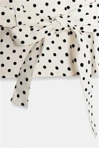 Detailopname van de elegante strik in de taille van een wit jasje met zwarte stippen