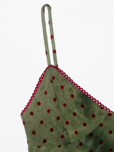 Close-up of red polka dot mesh fabric and scalloped lace trim on green dress strap