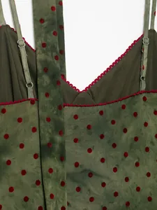 Close-up detail of olive green camisole dress featuring red polka dots and lace trim
