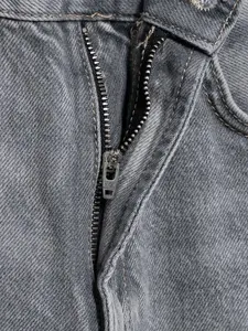 Detailaufnahme des hochwertigen Metallreißverschlusses einer grauen High-Waist-Jeanshose