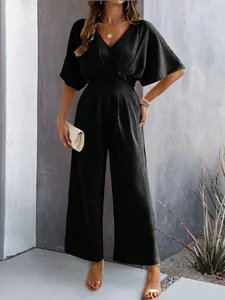 Elegant black V-neck wide-leg jumpsuit styled with gold jewelry and a beige clutch