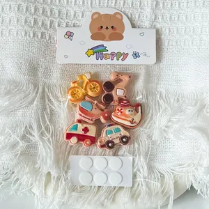 Close-up view of cute cartoon vehicle resin accessories including adhesive dots for DIY