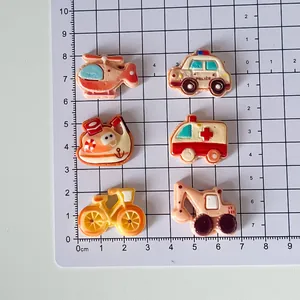 Detailed view of cartoon vehicle resin charms on a grid mat for DIY accessories