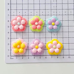 Six colorful glossy resin flower accessories on a white centimeter scale cutting mat.