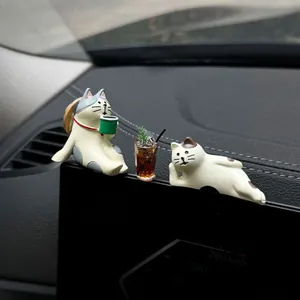 Close-up of miniature healing cat figurines with coffee for car dashboard decor.