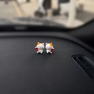 Close-up detail of two miniature lucky cat figurines sitting on a textured car dashboard