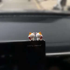 Close-up view of two cute white lucky cat ceramic figurines decorating a car dashboard screen