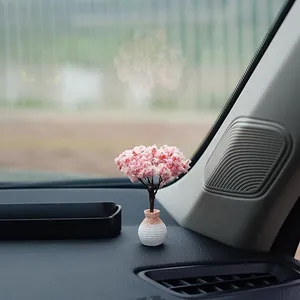 Elegant miniature pink cherry blossom simulation tree ornament placed on black car dashboard