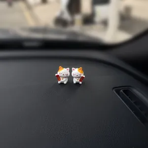 Two cute Maneki-neko lucky cat figurines sitting on a textured car dashboard