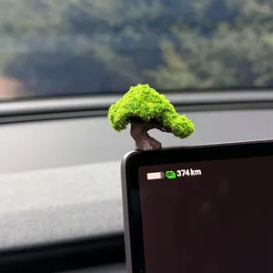 Detailed close-up of a miniature artificial bonsai tree on a car dashboard screen.