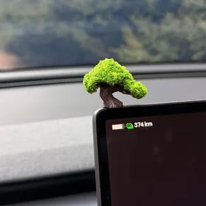 Close-up of a miniature artificial bonsai tree ornament on a car dashboard screen