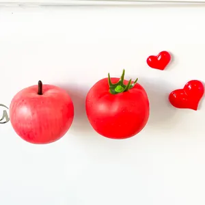 Detailed view of artificial red apple and tomato fridge magnets on white background.