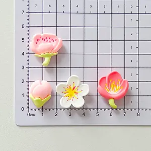Detailed view of handmade cherry blossom resin charms on a centimeter measurement grid