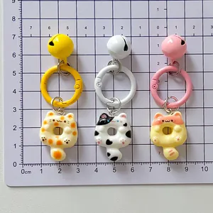 Detailed view of three cat-shaped donut keychains with bells on a measurement mat