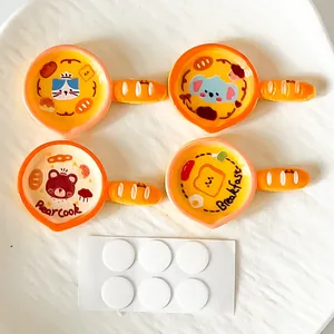 Close-up detail of four colorful cartoon resin frying pan charms with adhesive dots
