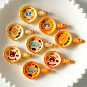 Close-up of various cartoon miniature frying pan resin fridge magnets on a white plate.