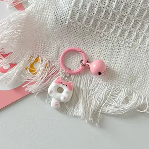Close-up of a cute pink and white cat donut keychain charm resting on a white textured fabric