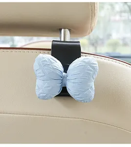 Close-up of a cute blue bow car seat back hook installed on a beige leather headrest.