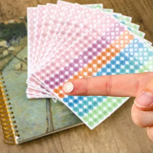 Close-up of a finger holding a silver-stamped colorful date dot sticker for planners