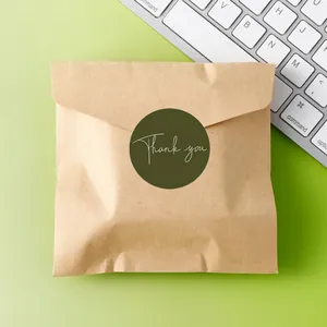 Detail of a 5cm round dark green Thank You sticker sealing a kraft brown paper envelope.