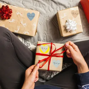 Detail showing colorful heart-shaped Thank You stickers on brown gift boxes with red ribbon
