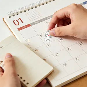 Macro view of a heart-shaped period tracker sticker being placed on a paper calendar
