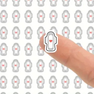 Close-up of a white menstrual tracking planner sticker with red heart held on a fingertip