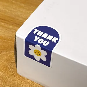 Vista detallada de una pegatina azul de Thank You sellando la esquina de una caja de regalo blanca