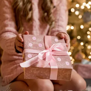Decorative pink and white swirl candy stickers on a pink gift box held by a child at Christmas