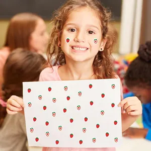Niña alegre mostrando una hoja de pequeñas pegatinas de frutas de fresa y corazones