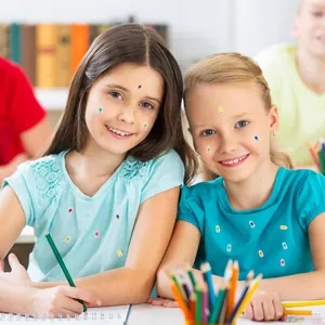 Colorful pencil reward stickers for teachers on children's faces and clothes in classroom.
