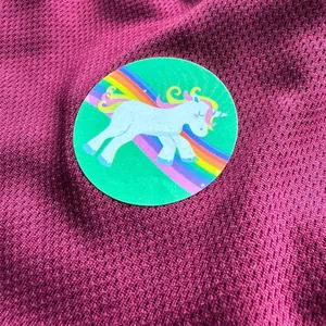 Close-up of a circular unicorn sticker with a rainbow pattern on dark red mesh fabric