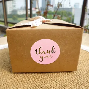 Pink thank you sticker with gold foil lettering on a kraft gift box