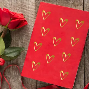 Detail shot of gold foil heart stickers applied to a red journal with a rose.
