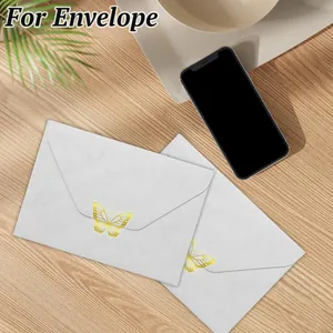 Close-up of gold foil butterfly stickers sealing white envelopes on a wooden desk